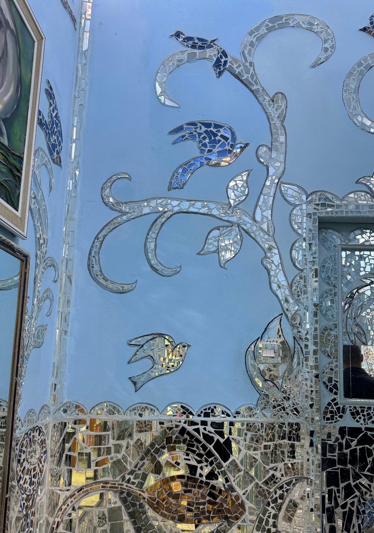 طيورٌ من المرايا بين أغصانٍ مورقة على جدارٍ أزرق