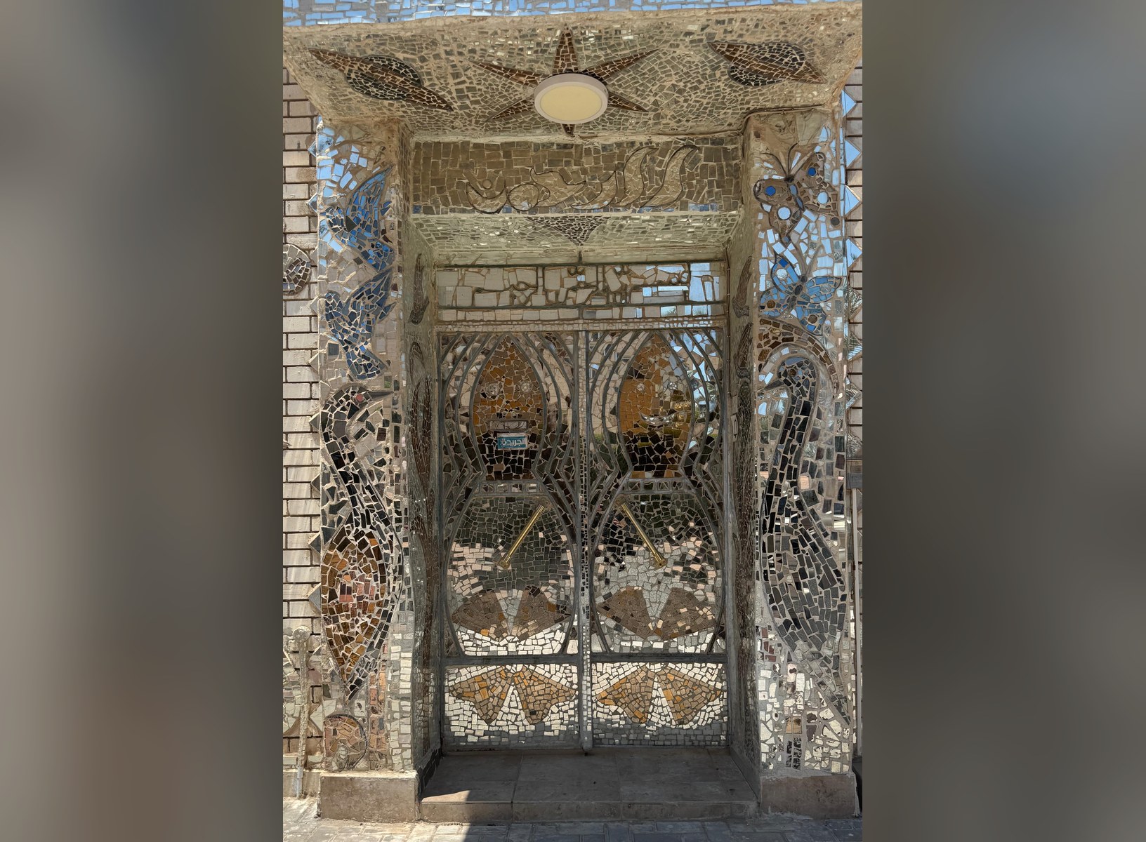 The twin mirror-mosaic entrance doors of The Mirror House beneath a mosaic sun relief