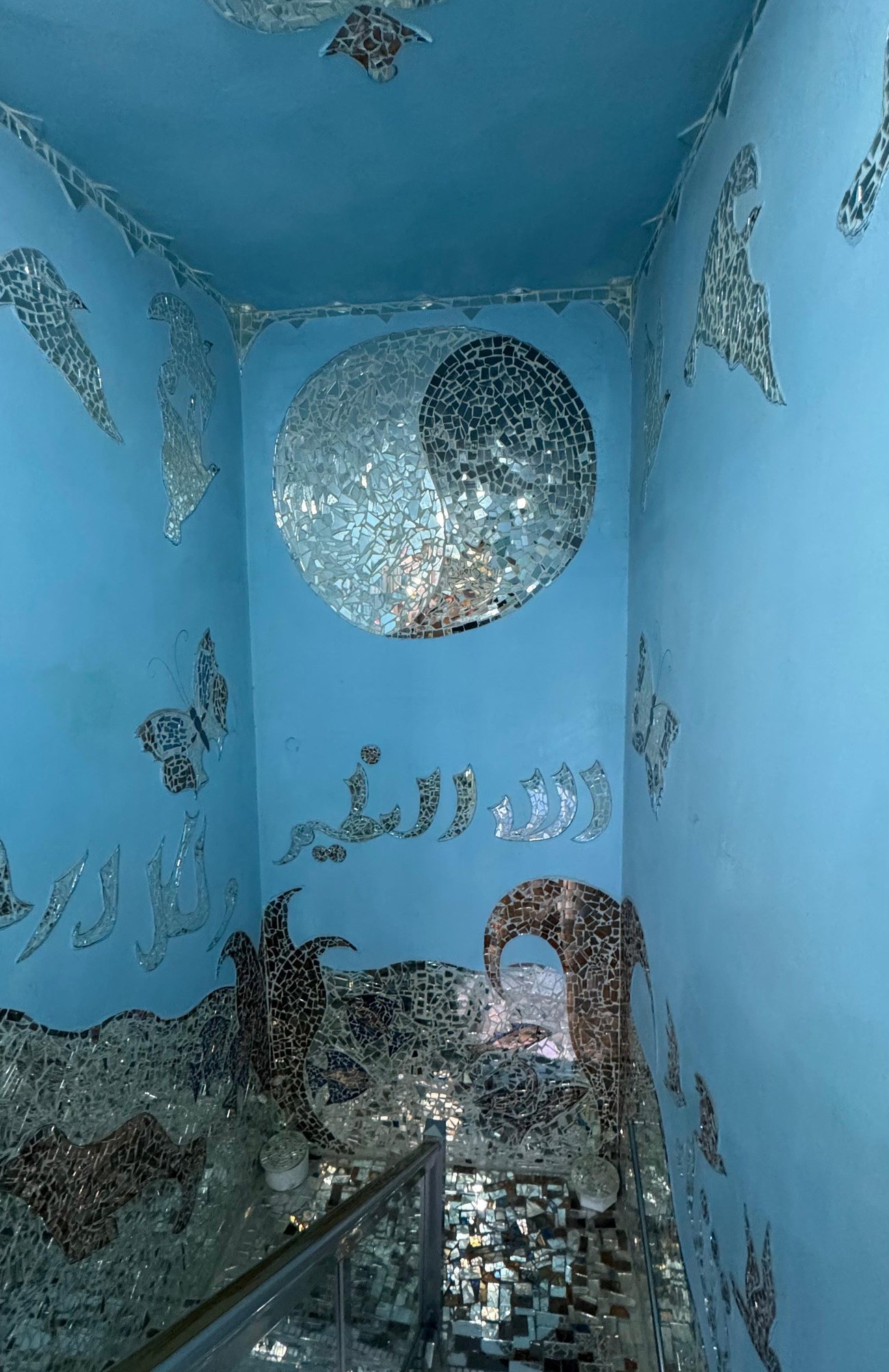 درجٌ أزرق تحت ميدالية دائرية من المرايا، فوق أمواجٍ وخطٍّ عربي